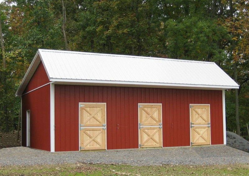 An image of a striking red metal building with a white door and a white roof. The building's bold color scheme adds a sense of character and personality to the scene, while the white door and roof create a sharp contrast, drawing attention to the entrance and the building's overall shape. This may be a residential or commercial space, with a design that combines traditional barn elements with modern features