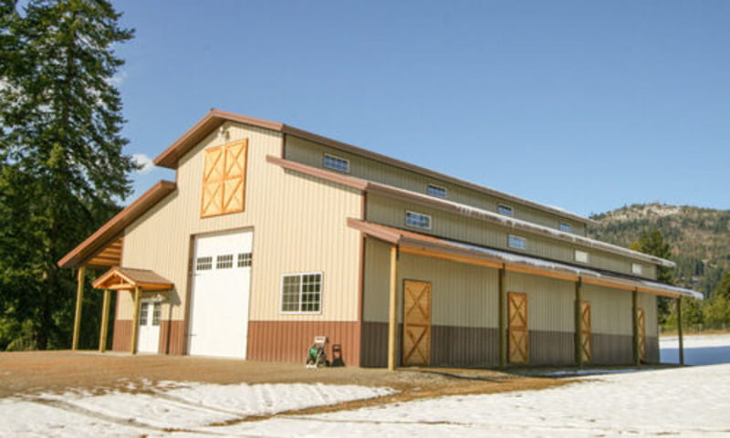A picturesque peach agricultural barn barndominium sits amidst a verdant landscape. The building's small brown windows offer a warm contrast to the bright peach exterior, creating a harmonious look. The large white garage door provides ample space for vehicles and equipment, making it a practical and attractive space for those in the agricultural industry.