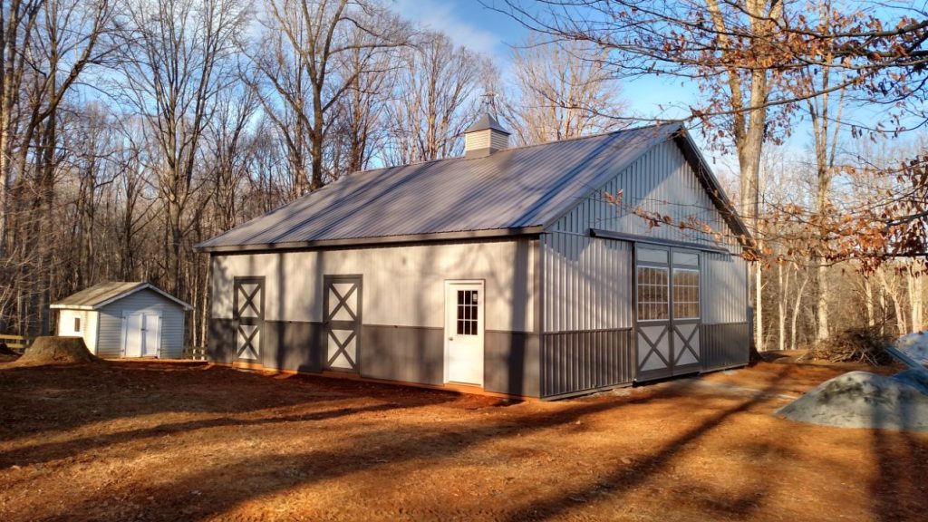 An image displays a cozy light brown equestrian metal building with a crisp white door as the focal point. The door is framed by the barndominium's light brown roof, creating a harmonious contrast. The barndominium's rustic design and natural hues evoke a sense of comfort and relaxation, perfect for those with a passion for horseback riding.
