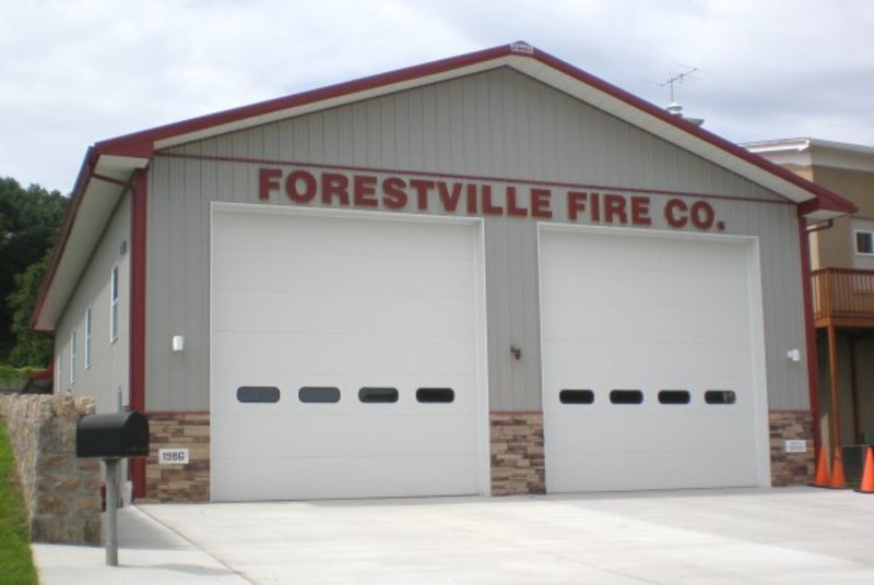 An image of a sleek grey and white fire department metal building. The building features two large white doors, providing easy access for fire trucks. The modern color scheme of grey and white creates a professional and functional appearance