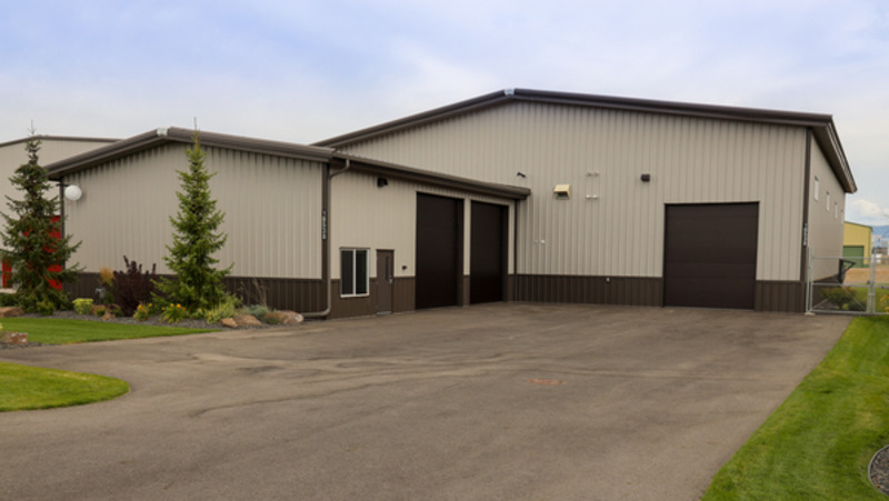 A large light brown commercial barndominium takes center stage in this image, showcasing its modern and professional design. The building's small windows provide a perfect balance of natural light and privacy. The big three brown garage doors offer ample space for vehicles and storage, making it an ideal space for a variety of businesses.