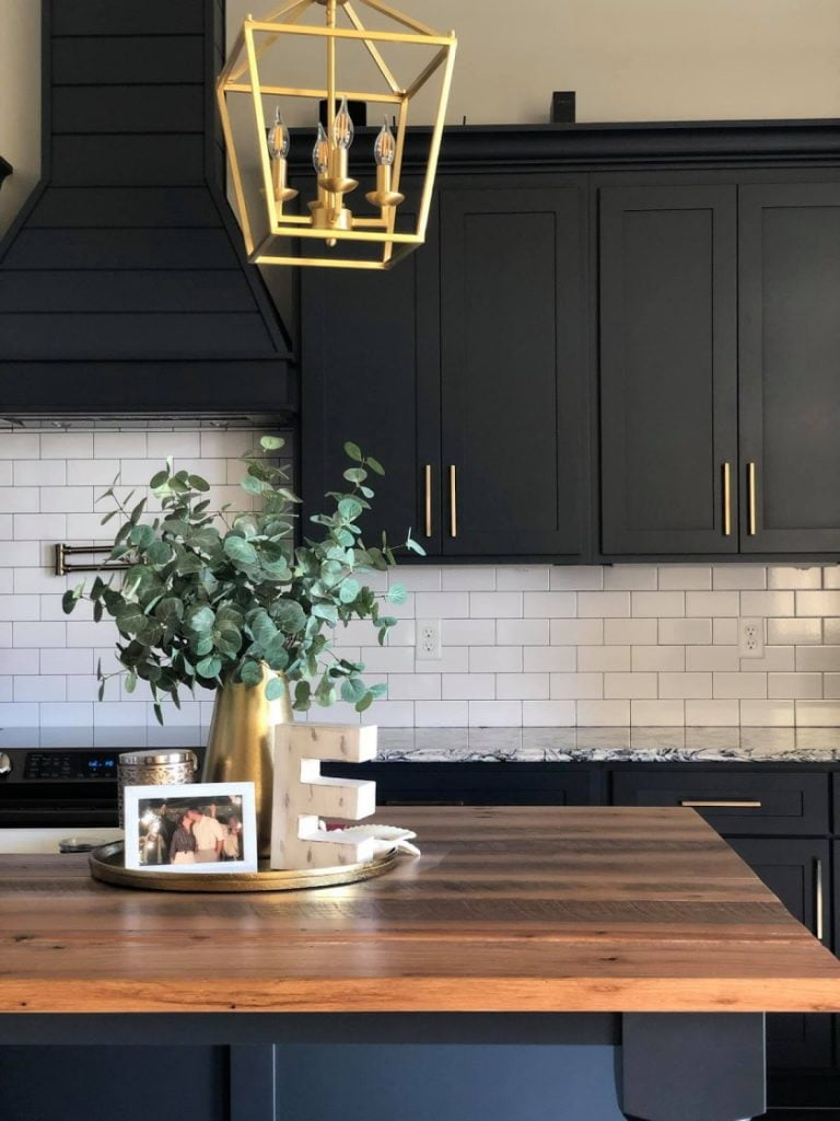 A photograph of a kitchen with a dramatic black and gold color scheme. The cabinets and drawers in the kitchen are made of a sleek black material, with a glossy finish that reflects the light and adds depth to the space.