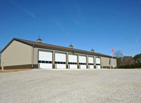 "An image of a brown general steel building located in Colorado, standing tall against a clear blue sky. The rectangular structure has a flat roof and is made of sturdy steel panels with a textured surface. The building's facade is a deep shade of brown, with no visible windows or doors from this angle. Surrounding the building is a vast open space with greenery, indicating it may be situated in an industrial or commercial area.