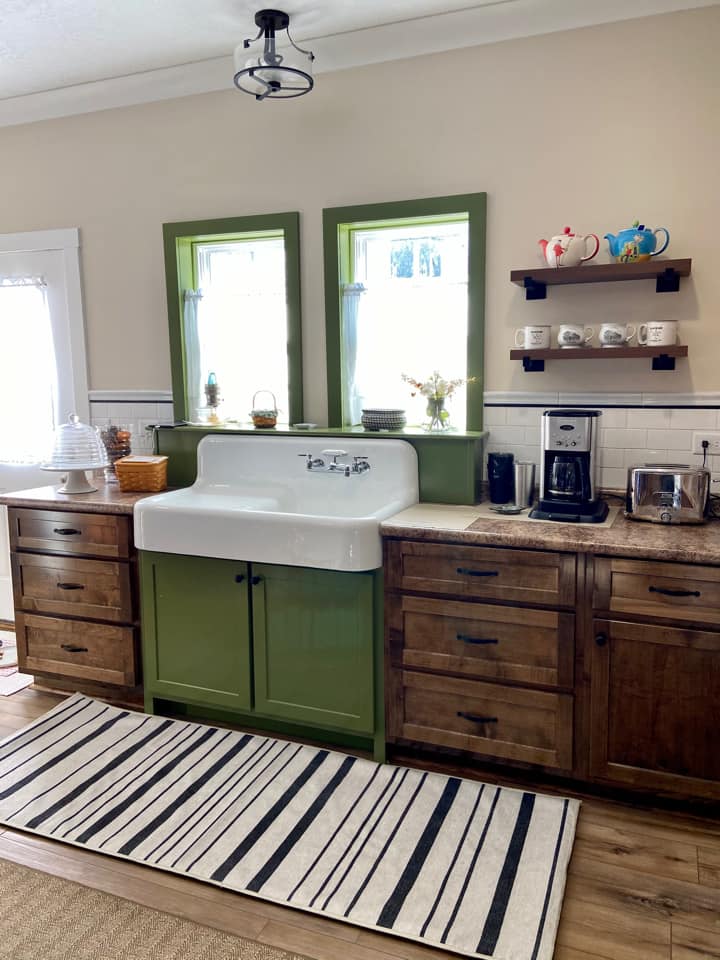 A cozy kitchen featuring wooden drawers and cabinets with sleek metal handles. The countertops are a light beige color, and there is a vibrant green sink in the center of the image