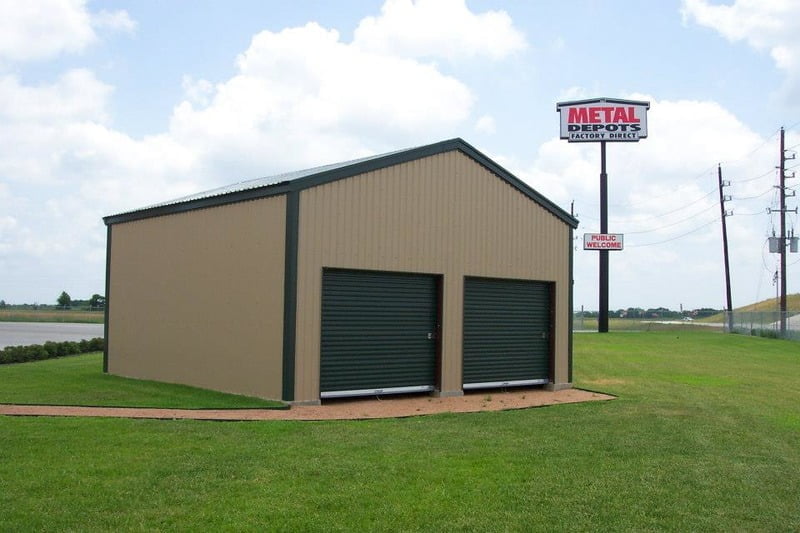 An aerial view of a brown commercial metal building with a large rectangular shape and a flat roof. The building has multiple windows and doors, and a spacious parking lot with several cars and trucks parked in front of it. The metal panels on the building's facade have a smooth texture, and the overall design appears modern and functional. The surrounding landscape is mostly grass and trees, creating a natural contrast to the man-made structure.