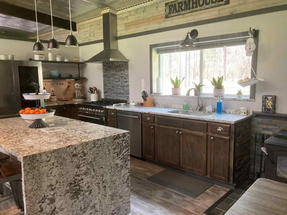 An image of a sleek and modern kitchen with a minimalist design. The space features clean lines, simple shapes, and a neutral color palette that creates a sense of calm and order. The kitchen is well-lit with recessed lighting, highlighting the smooth surfaces and reflective finishes. The countertops and backsplash are made of a high-gloss material, giving the kitchen a polished and sophisticated look.