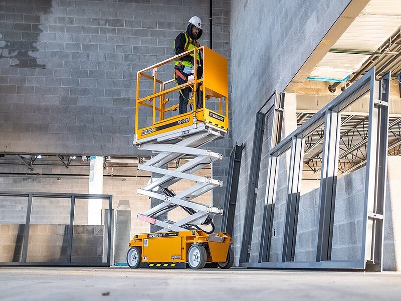A sleek electric scissor lift positioned on a construction site against a backdrop of scaffolding and building materials.