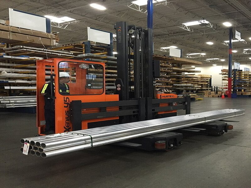A side loader forklift in action, featuring a sturdy metallic frame with orange accents.