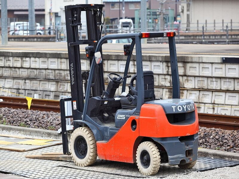 A red forklift, with a sturdy frame and four wheels, stands tall against a backdrop of a bustling warehouse.
