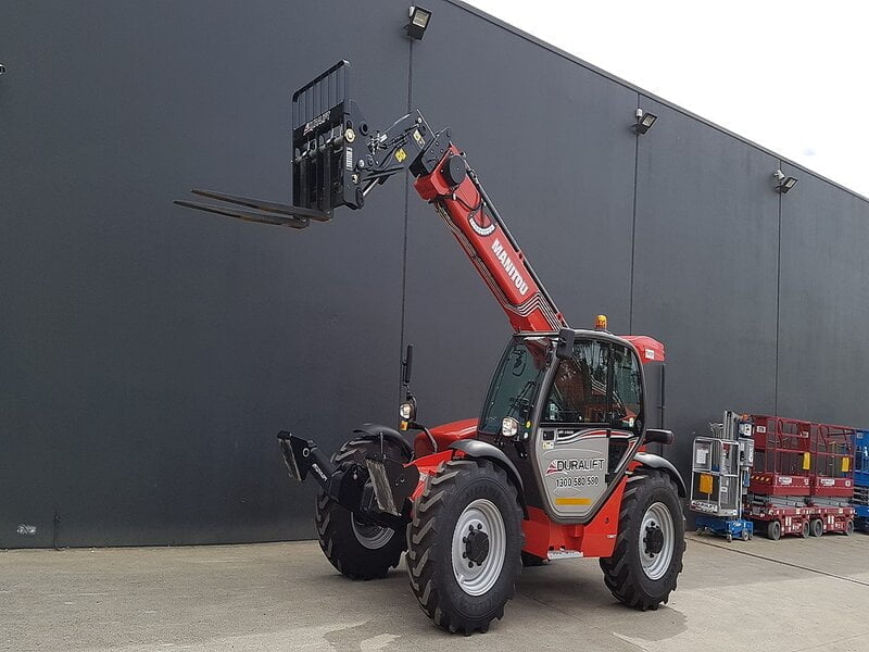 A sturdy telehandler forklift stands tall against a backdrop of a bustling warehouse. 