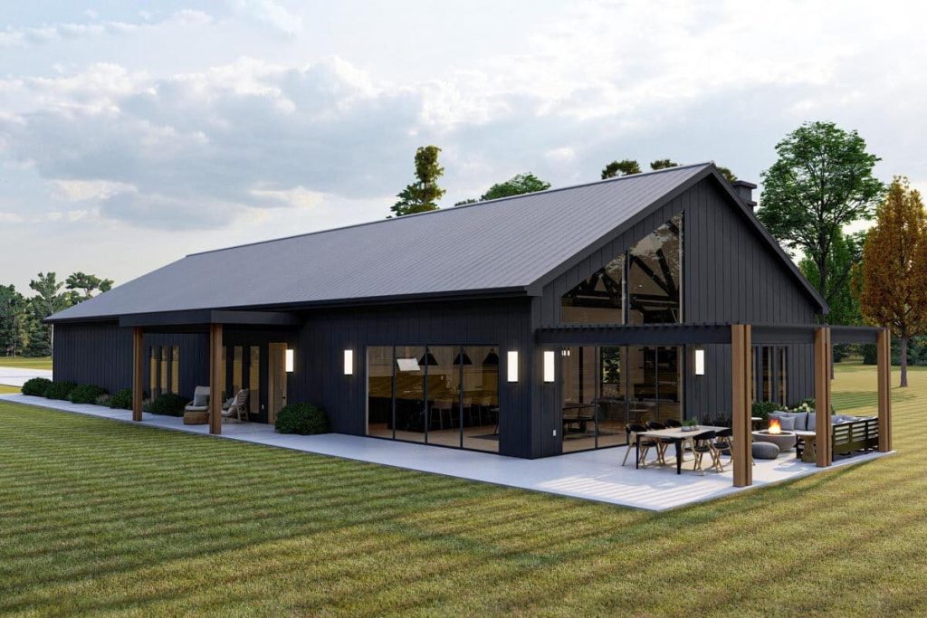 An angled right view of the barndominium 3-bed plan showcasing its appealing board and batten siding. The structure boasts a standing seam metal roof and is adorned with a spacious pergola. Abundant natural light floods the interior through large windows on two sides, seamlessly blending the indoors with the surrounding outdoors.