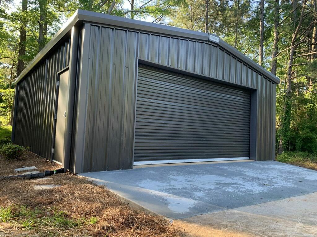 A black 30×30 metal garage set on a concrete foundation with trees in the background
