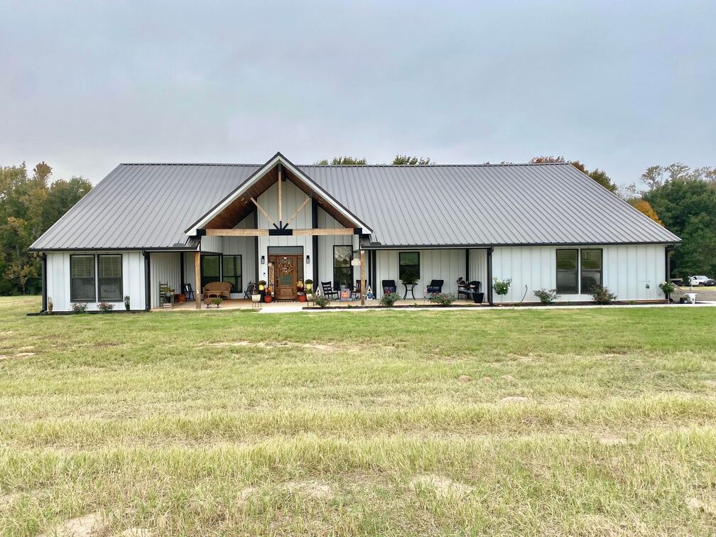 A beautiful white and gray barndominium with an expansive green lawn