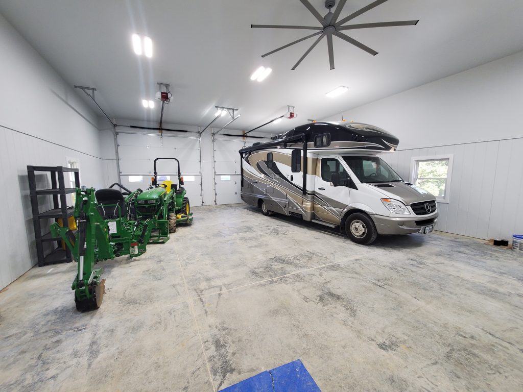 The white interior of a large 3-car garage with a green mini excavator and an RV parked inside