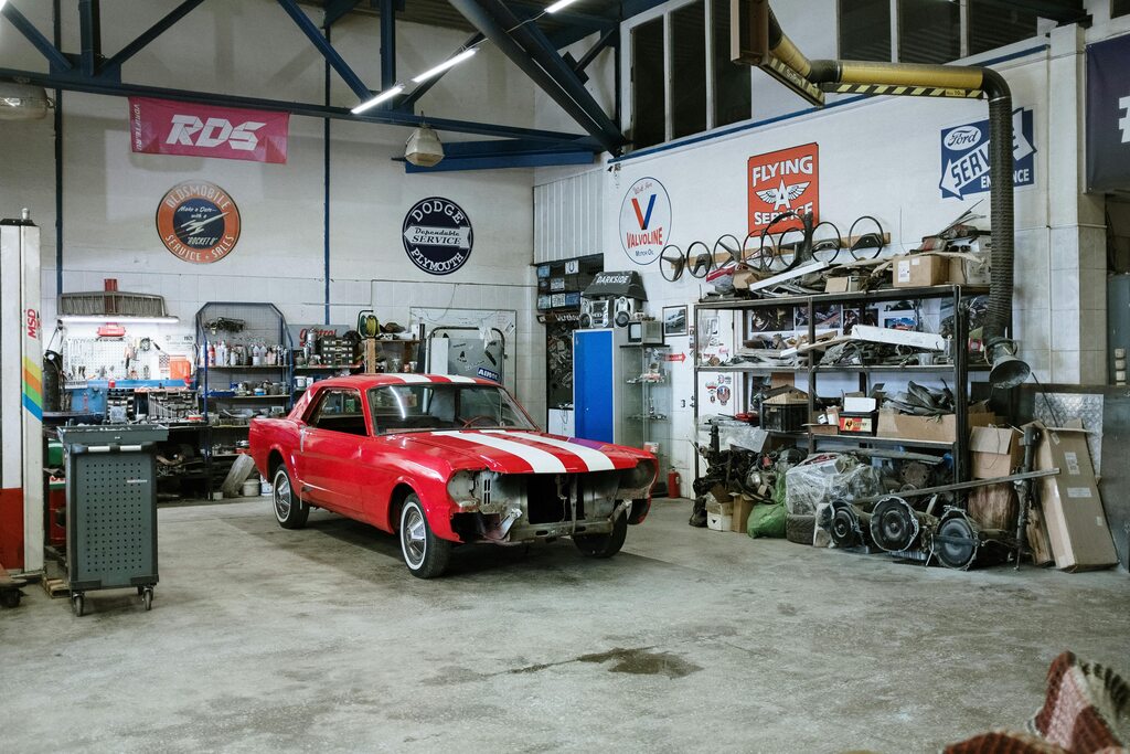 The interior of a large white garage with a red car and spare parts