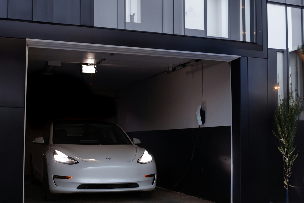A black and white and white open attached garage with a parked Tesla Sedan inside.