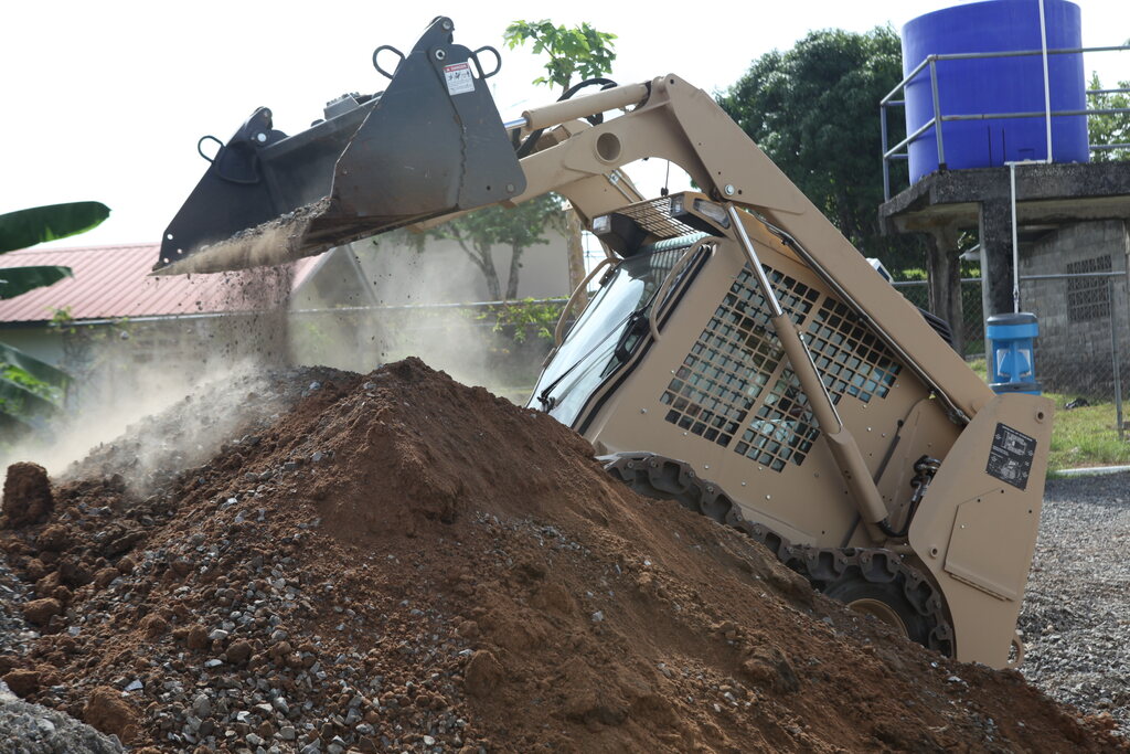 A Yellow Bobcat skid steer loader clearing soil at a construction site.