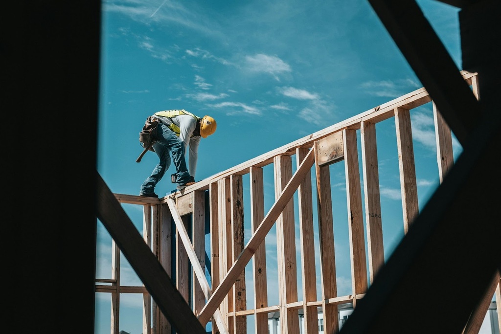 A construction worker on top of the wooden frame of a bardominium which he is building
